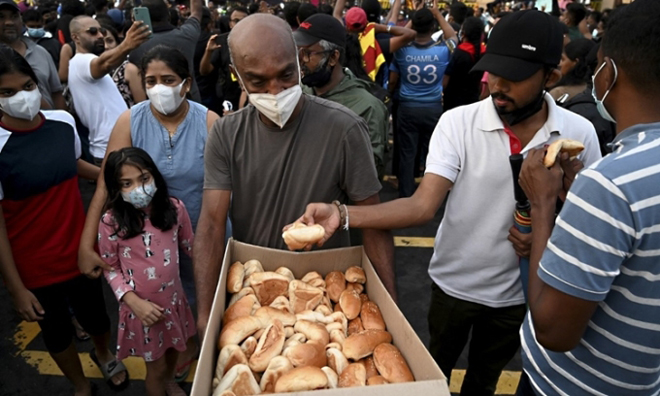 Một người đàn ông phát bánh mỳ cho đám đông tham gia biểu tình bên ngoài văn phòng Tổng thống Sri Lanka ở Colombo. Ảnh: AFP.